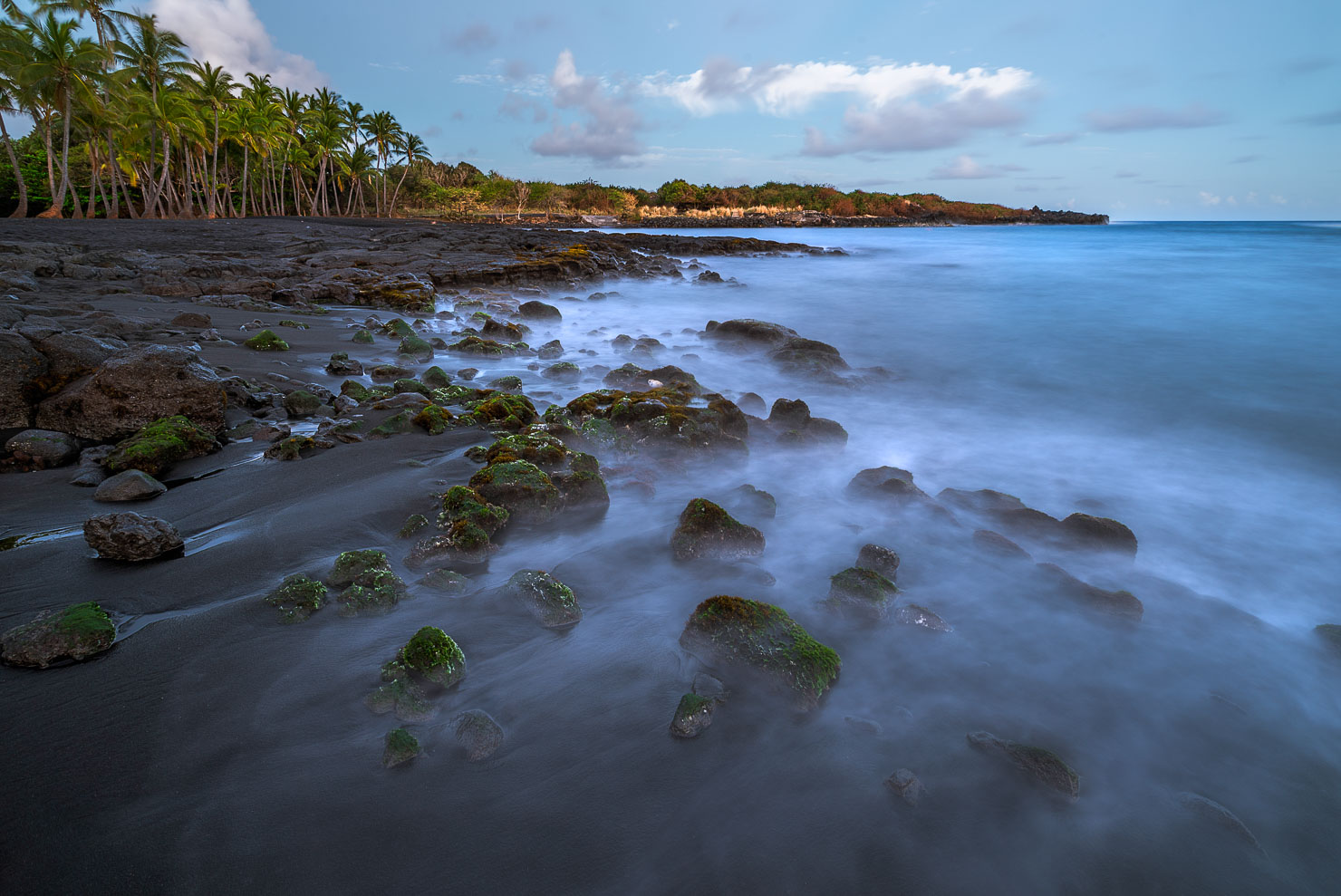 Long exposure of black sand beach with silky water and mossy rocks, Hawaii