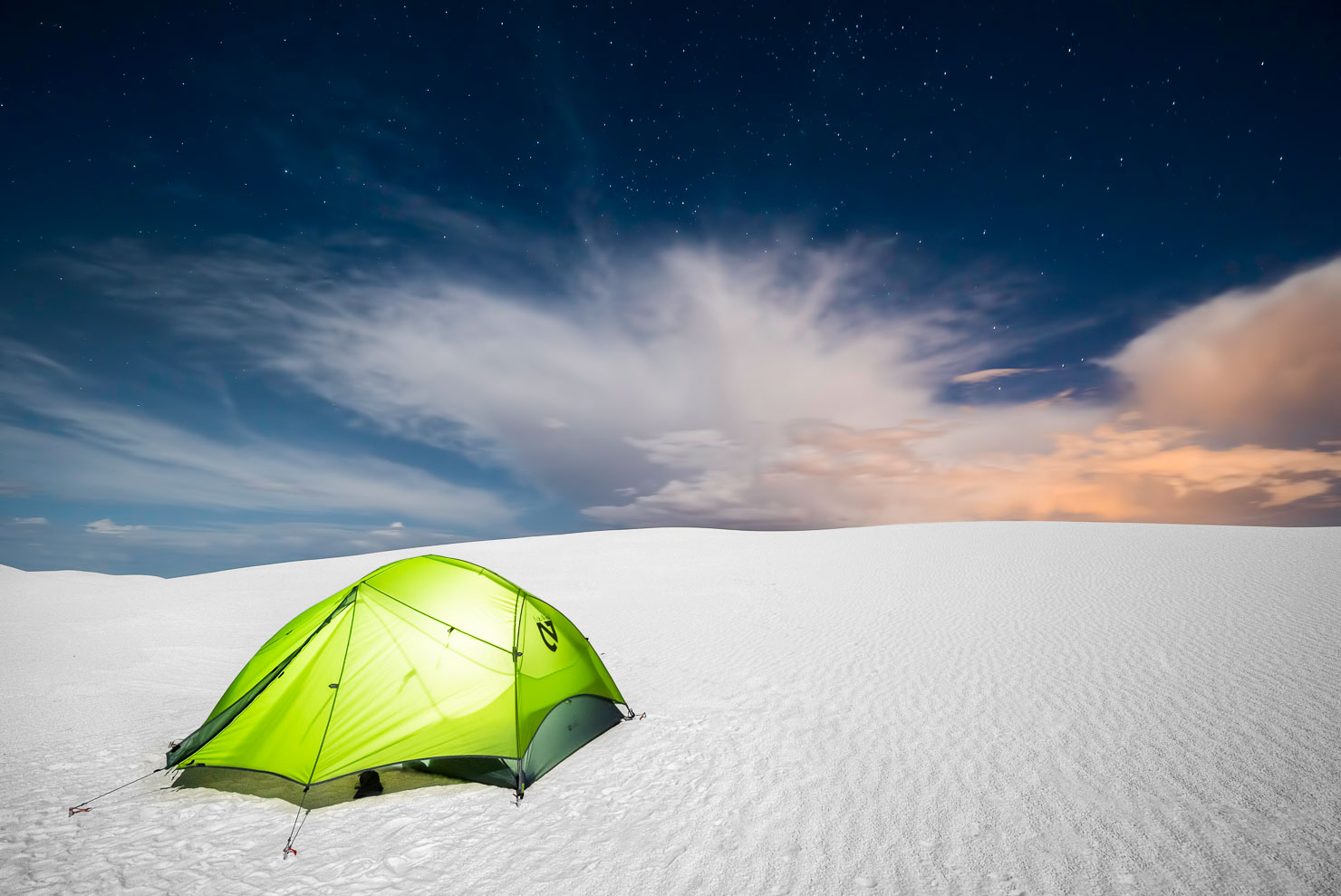 Green tent glowing under night sky at White Sands, New Mexico