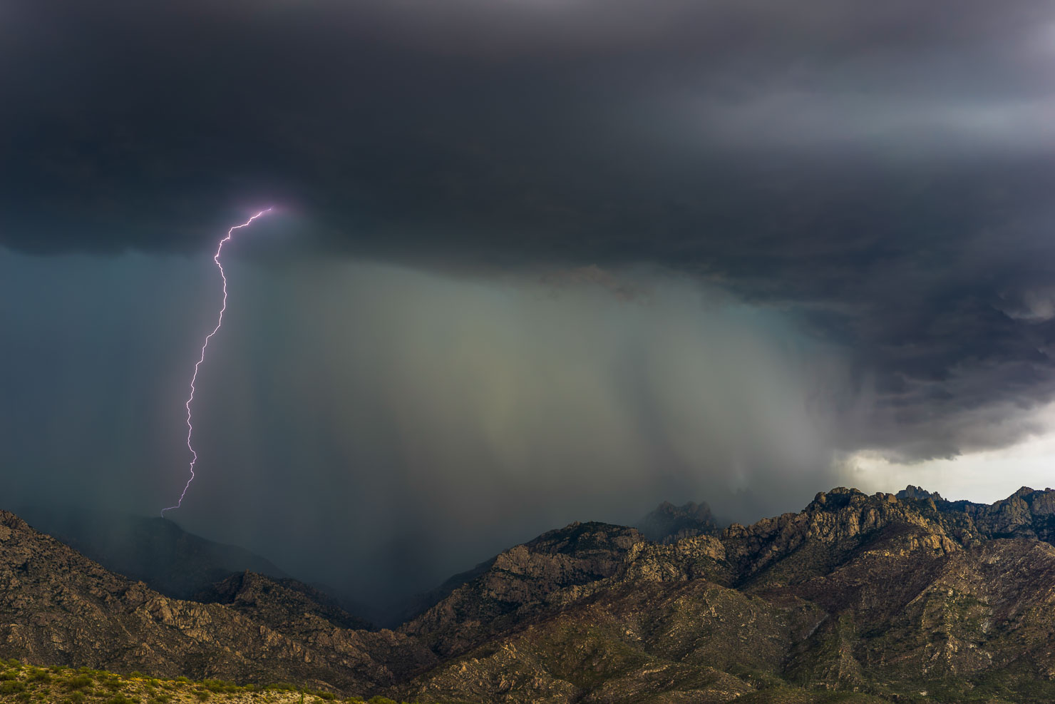 Lightning bolt striking over rocky mountain range under dramatic storm clouds